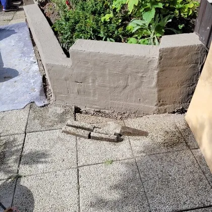 Nyputsad stödmur i en villaträdgård i Flen intill en stensatt uteplats och grönskande rabatt.