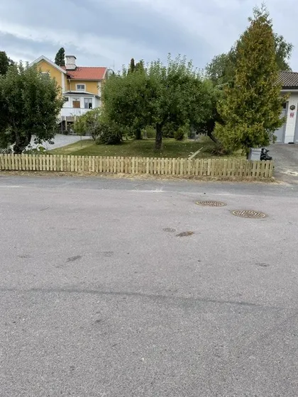 Renoverat trästaket i naturträ längs en villagata i Flen