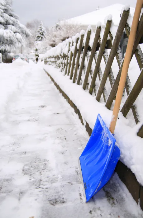 Snöskyffel vid skottad gångväg och trästaket efter snöskottning i Malmköping.